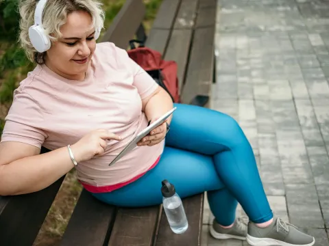 A Woman Sits on a Park Bench Scrolling Through Her Tablet Listening to Music