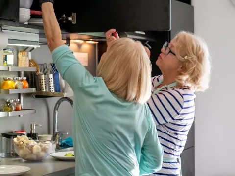 A Couple of Friends Get Ingredients From a Cabinet in the Kitchen as the Duo Prepares to Cook.