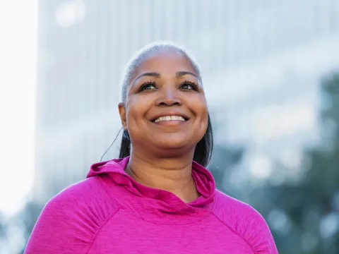 A smiling woman outside wearing a pink shirt for breast cancer awareness.