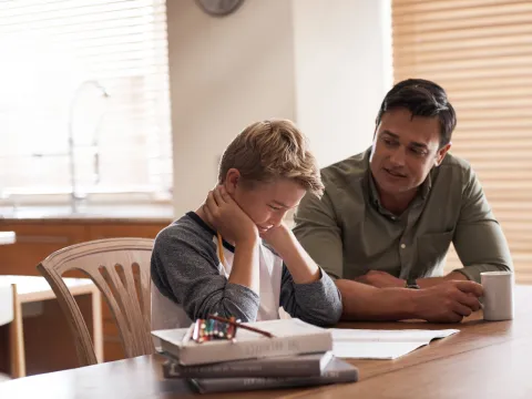 A Child Sits at the Kitchen Table Frustrated with School Work as His Father Tries to Help.