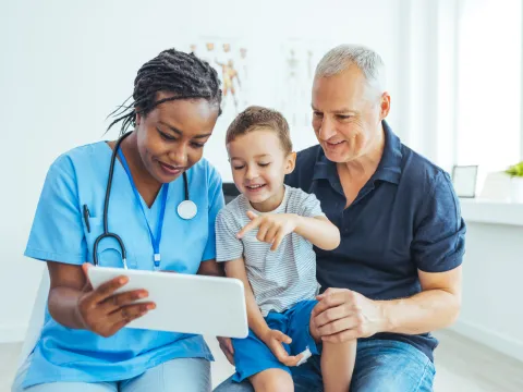 A Doctor Reviews a Patient's Chart with a Pediatric Patient and His Father in an Exam Room.