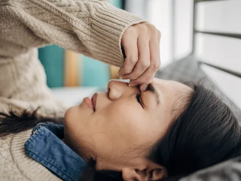 A Woman Squeezes the Bridge of Her Nose While Laying Down at Home