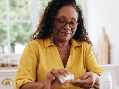 A Woman Sits at the Kitchen Table and Shakes a Pill Out of a Bottle