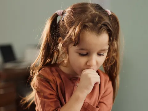 A Little Girl in Pig Tails Covers Her Mouth While Coughing