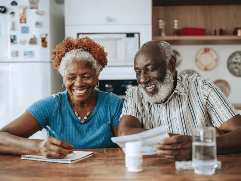 Man and Woman Sitting at Table Tracking Medications in Notebook