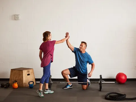 A Caucasian man and woman high-five while exercising at the gym.