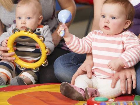 Two infants seated on the, held by their parents, holding baby instruments