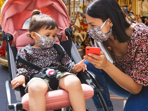 A mom and her young daughter wearing masks at a theme park.