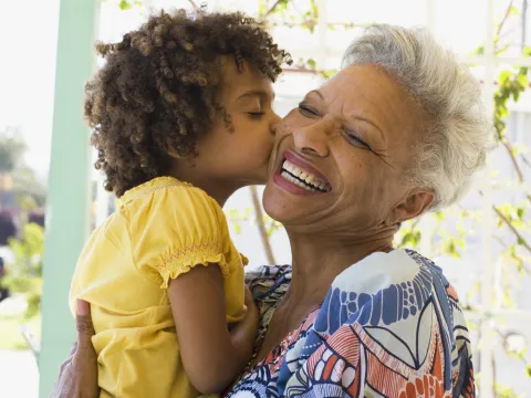 A grandmother holding her grandchild, who is giving her a kiss on the cheek.