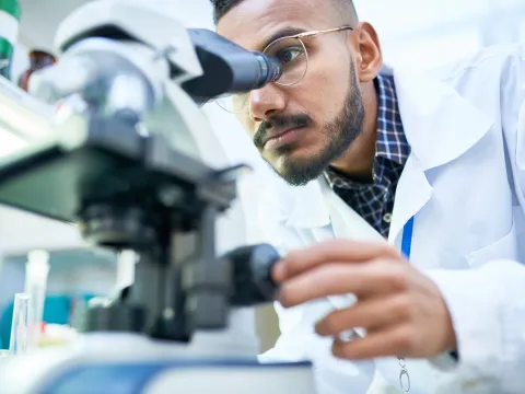 Man looking into a microscope to analyze the results of a clinical trial.