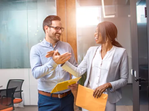 Two coworkers, laughing, smiling, and clapping hands together.