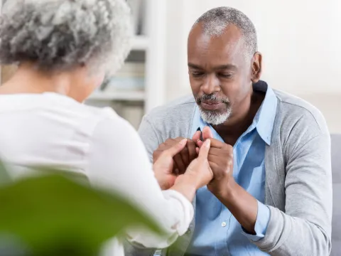 Elderly couple sitting across from each other, clasping hands, and praying together.