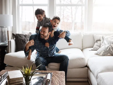 A father and his two sons playing on the sofa of their living room.