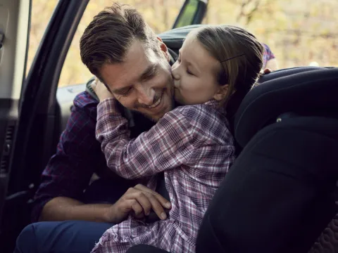 A dad buckles his daughter into a carseat in the backseat of a car.