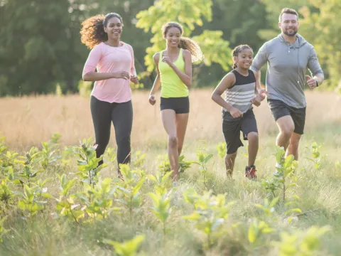 A family of four, running together outside in a field.