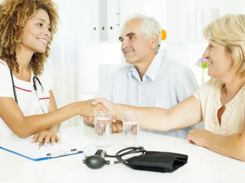 Senior couple discussing heartburn with their doctor. They are all sitting at a table and the doctor is grasping hands with the wife.