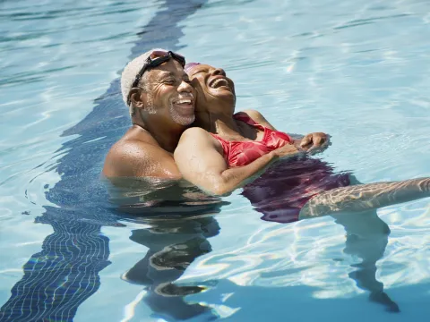 An adult African American couple swims in a pool on a hot day.