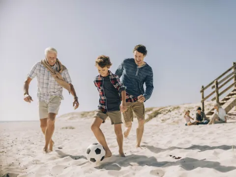 A family plays soccer on the beach.