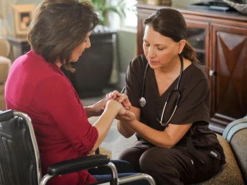 Woman in a wheelchair praying with a nurse.