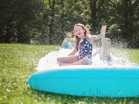 Happy children play on a slip and slide outside on a sunny day.
