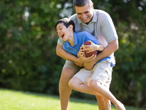 A father and son play football outdoors.