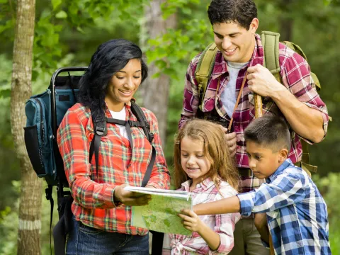 A family reads a map together while hiking in the woods.