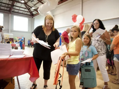 A woman giving school supplies to two little girls.