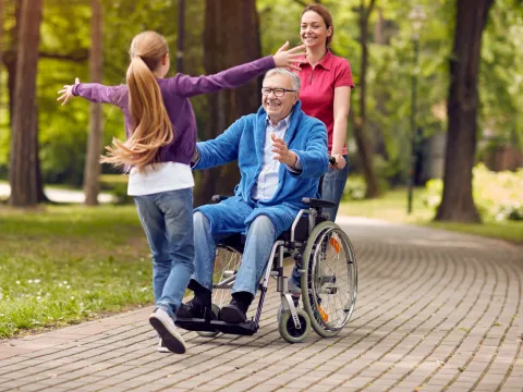 A grandfather and granddaughter hug outside.