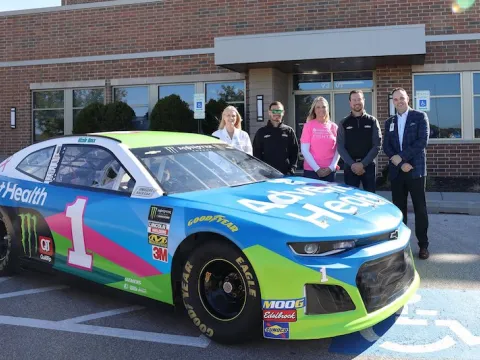 People standing next to the AdventHealth branded Nascar