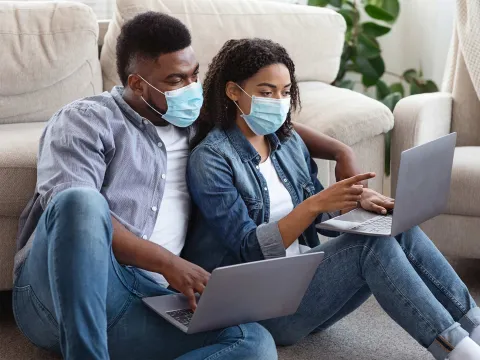 A couple wearing masks using their computers.