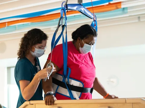 Physical therapist helping a patient in rehab with a walking exercise with the patient is being supported by a harness.