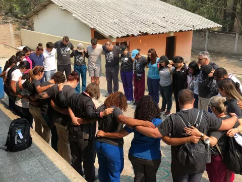A group of doctors, employees, and volunteers in a circle of prayer
