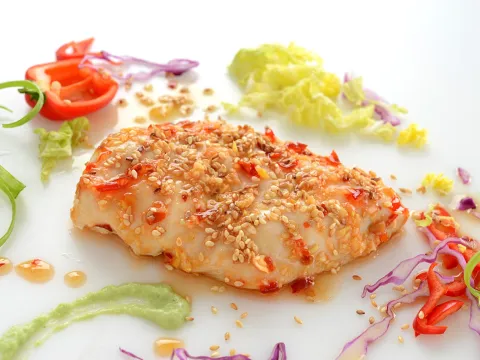 a serving of prepared chicken, coated in sesame seeds and surrounded by shredded cabbage