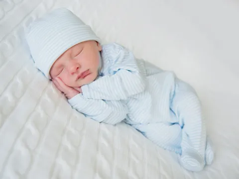 Newborn in blue clothes and a blue hat on a white blanket