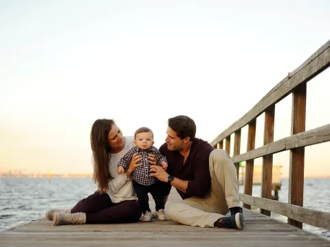 A young couple sitting on a dock holding their baby.