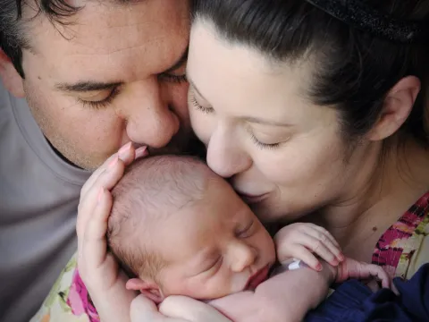 A couple holding and kissing their newborn baby.
