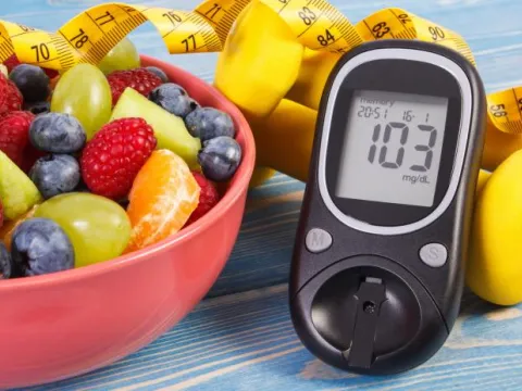 A Bowl of Fruit and a Glucose Checker Lay on a Countertop