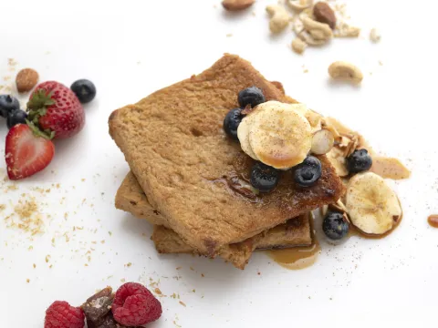 Three stacked slices of French toast with banana and berry garnishes