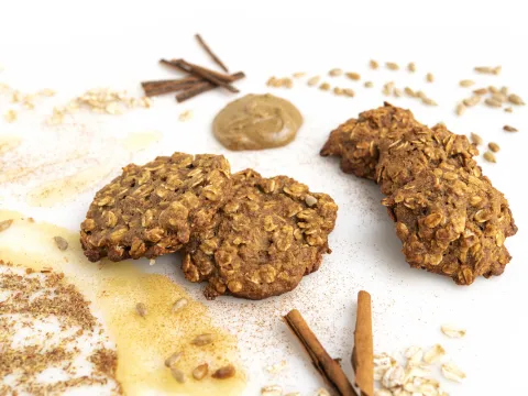 Five oatmeal cookies on a white surface with cinnamon sticks