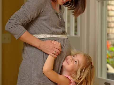 A young girl touches her pregnant mom's belly.