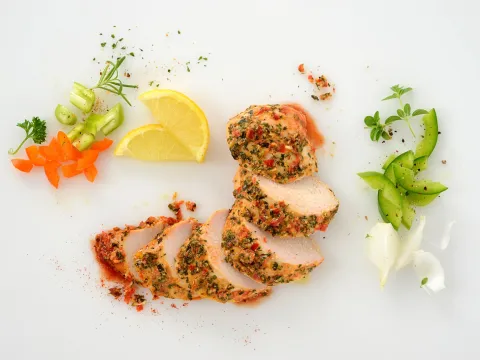 a sliced, chicken breast, surrounded by herbs, lemon, and veggies