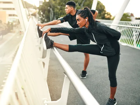 Two runners, stretching side by side, their legs extended and touching their toes.