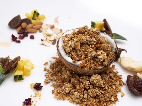 fresh baked granola, placed in half a coconut shell, surrounded by almonds, dates and pineapple chunks