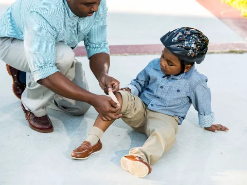 A father puts a bandage on his son's knee. 