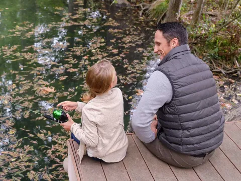 A father and daughter sitting on a pier while fishing