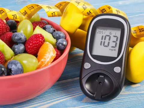 A bowl of fresh fruit next to a blood sugar monitor