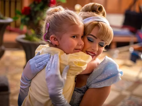 A little girl with a cochlear implant hugs Cinderella.