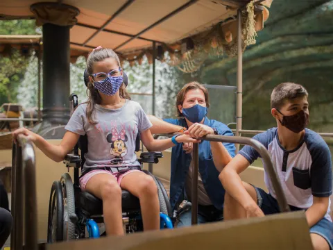 A young girl in a wheelchair and wearing a mask while riding Disney's Jungle Cruise ride.