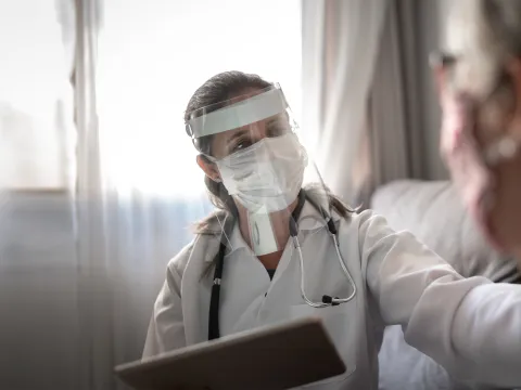 Doctor wearing PPE and talking with a patient that's wearing a mask.