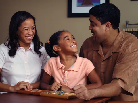 A daughter smiles at her father while playing a game with her parents. 